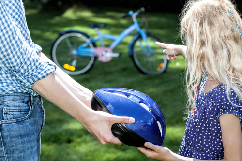 dad handing a bicycle helmet to his daughter